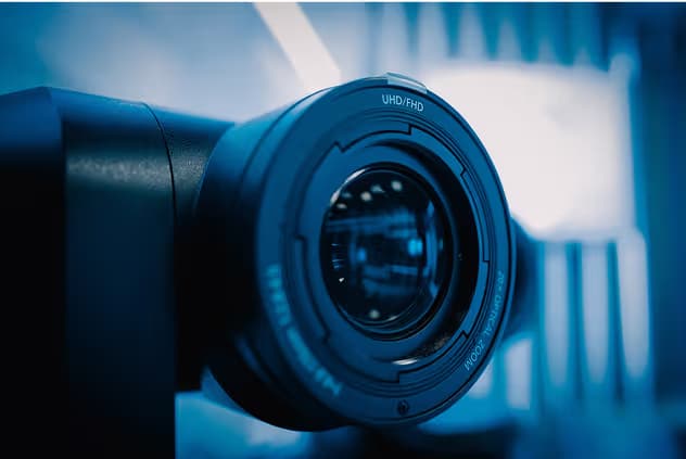 Close-up of a camera lens mounted on a black body, displaying UHD/FHD text on the lens rim, with a soft blue background.