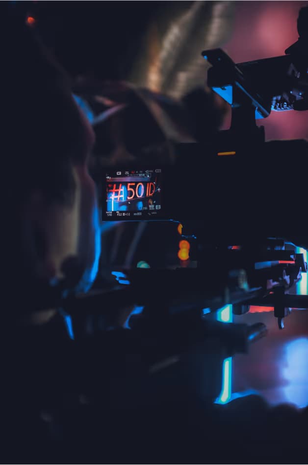 A close-up view of a camera setup with colorful lighting in the background. The camera display shows a readout of 50 ID, while a person is partially visible, focused on the equipment.